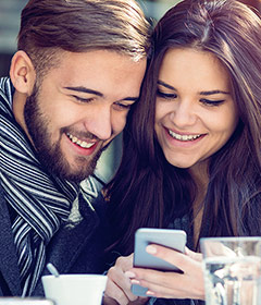 Una bella e giovane coppia di ragazzi navigano dal proprio smartphone in un caffè e sorridono.